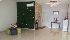 Un vestíbulo moderno y limpio con una pared verde decorada con flores, una mesa de recepción, un refrigerador y un cartel que indica la entrada.