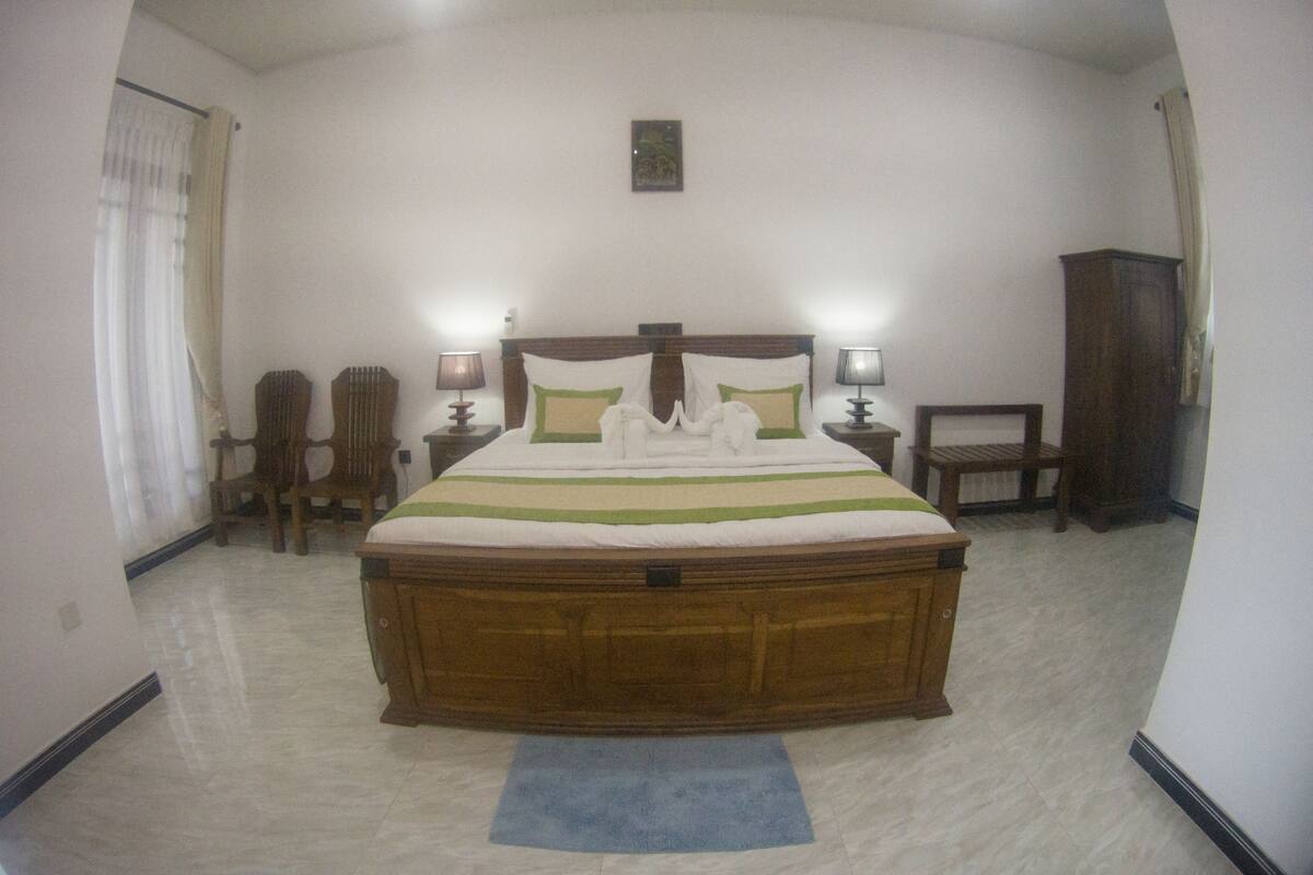 A bedroom with a large bed, two bedside tables with lamps, a wooden chair, a wooden cabinet, and a blue rug.