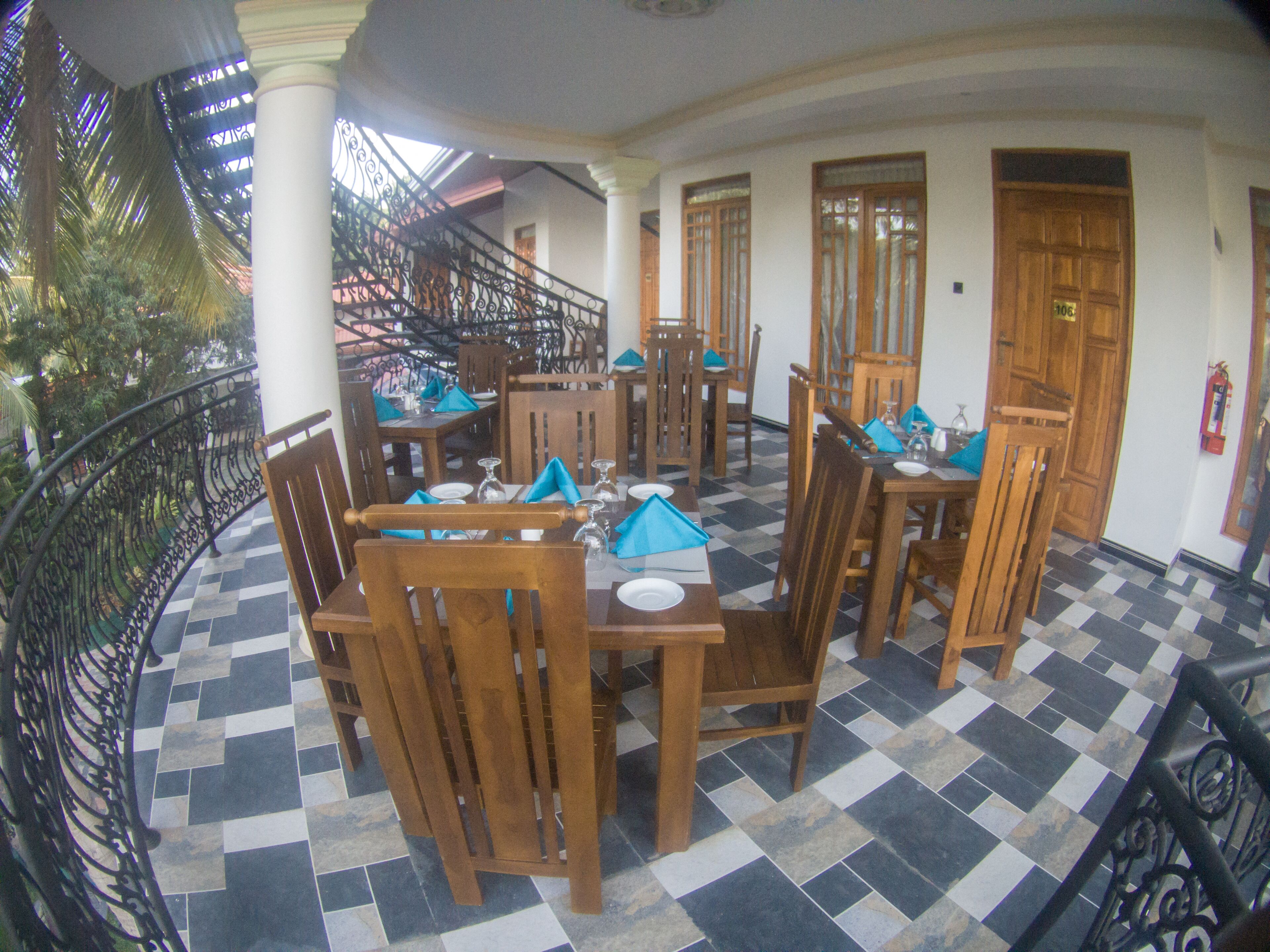 A dining area with wooden tables and chairs, checkered floor tiles, and a balcony with a wrought iron railing.