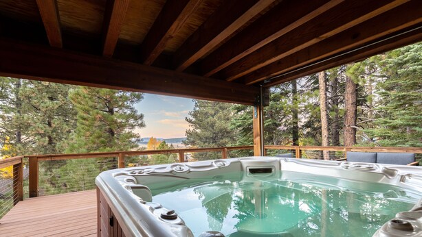 Ein Whirlpool auf einer Holzterrasse mit Blick auf Bäume und eine entfernte Landschaft.