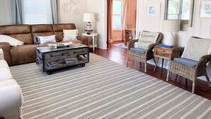 A living room with a brown leather sofa, a coffee table, wicker chairs, and a patterned rug. - Modern East Beach 3BR 2BA With Pool + Walk to Beach (St Simons)