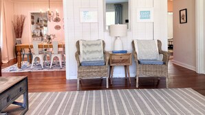 A cozy living room with wicker chairs, a wooden coffee table, and a dining area with a white table and chairs. - Modern East Beach 3BR 2BA With Pool + Walk to Beach (St Simons)