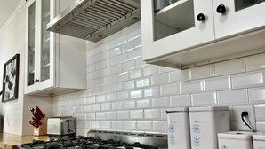 A modern kitchen with white cabinets, a stainless steel stove, and white tiled backsplash. - Modern East Beach 3BR 2BA With Pool + Walk to Beach (St Simons)