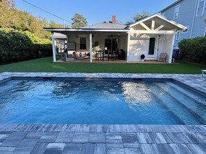 A swimming pool with a patio area, a covered outdoor seating area, and a house in the background.