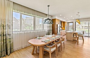 A modern kitchen with wooden cabinets, a central island, and a dining area with a round table and chairs.
