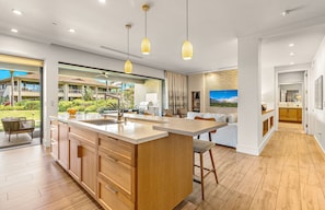 A modern kitchen with wooden cabinets, a central island, pendant lighting, and a view of the outdoor area.