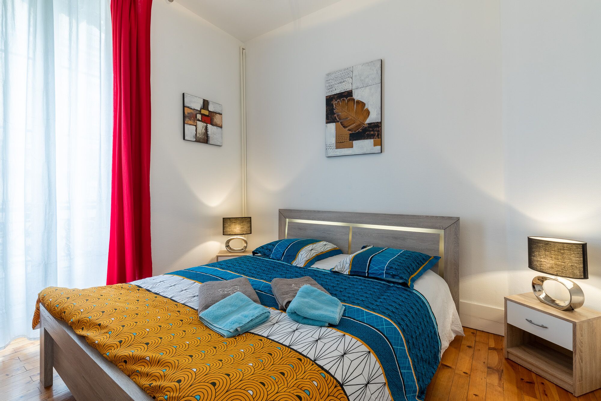 A modern bedroom with a bed, bedside tables, and artwork on the walls.