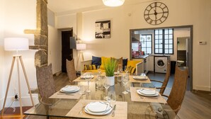 Un comedor con una mesa de vidrio preparada para seis comensales, un pilar de piedra y una cocina al fondo.
