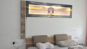 A bedroom with a wooden headboard, a painting of a house on a pier, a bedside table with a lamp, and a bed with patterned bedding. - Apartment overlooking the Grünten, on foot to the Great Alpsee (Bühl a.Alpsee)