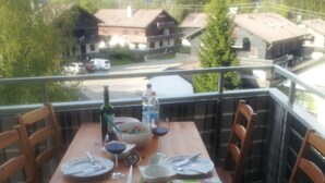 A wooden table set for four on a balcony with chairs, a bottle of water, a bowl of fruit, and a menu. - Apartment overlooking the Grünten, on foot to the Great Alpsee (Bühl a.Alpsee)