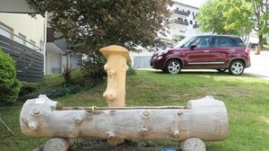 A wooden sculpture resembling a log with a face, placed on a concrete base in a grassy area with a red car parked nearby. - Apartment overlooking the Grünten, on foot to the Great Alpsee (Bühl a.Alpsee)