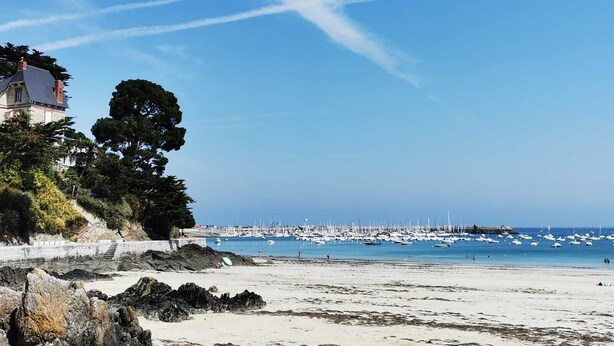 A coastal beach with a rocky shoreline, a building with a sloped roof, and a marina with numerous boats. - GITE LE COIN with swimming pool (Bonnemain)