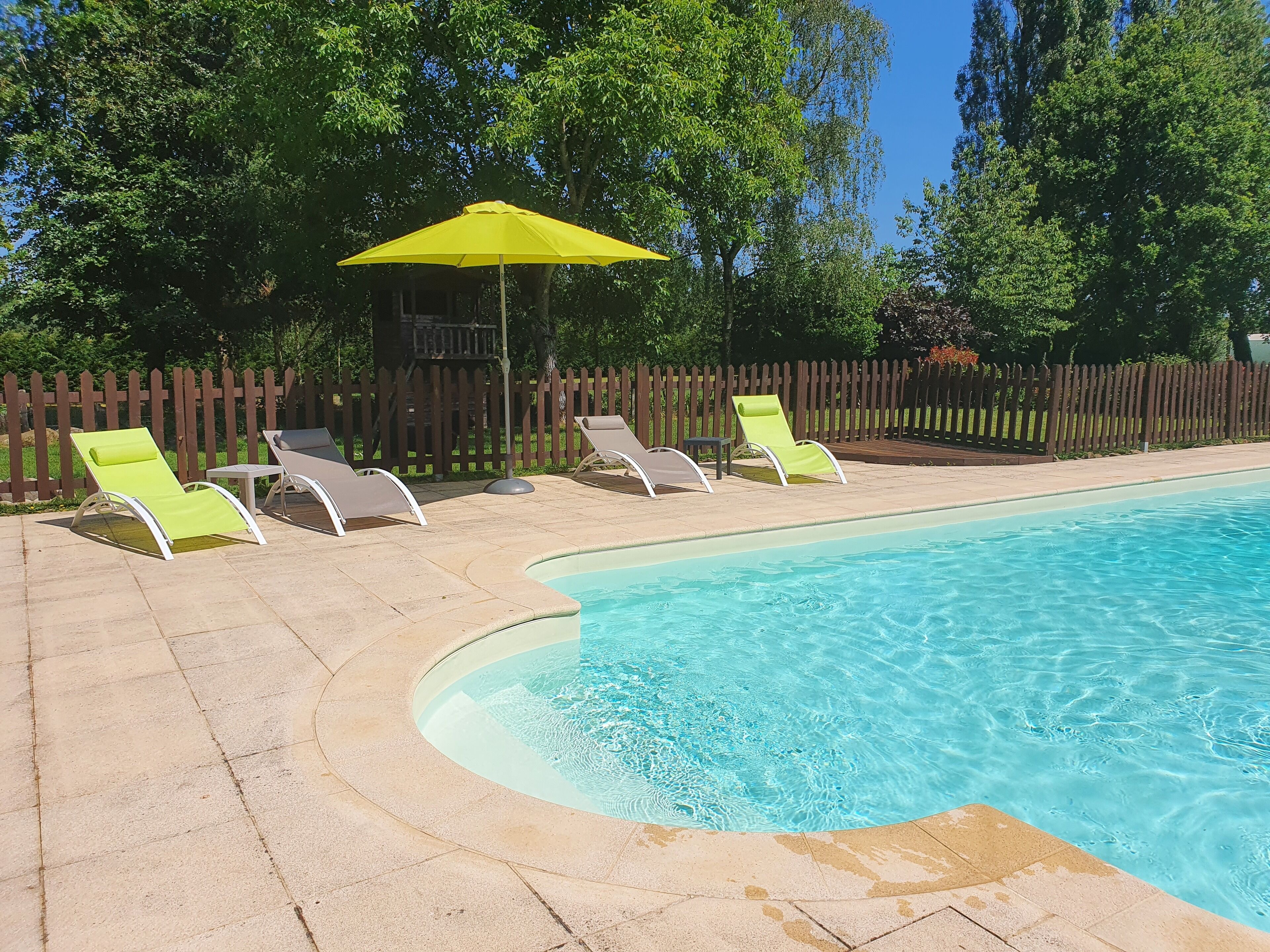 A swimming pool with a curved edge, surrounded by a wooden fence and trees.