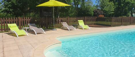 A swimming pool with a curved edge, surrounded by a wooden fence and trees.