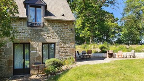 A stone house with a large window and a balcony, a patio with outdoor furniture, and a grassy yard. - GITE LE COIN with swimming pool (Bonnemain)