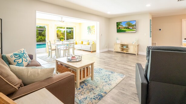 A spacious living room with a dining area, a sofa, a coffee table, and a TV mounted on the wall.