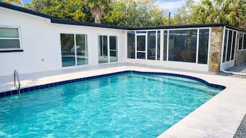 Una piscina con agua azul cristalina, rodeada por un edificio blanco con ventanas amplias y un pilar de piedra.