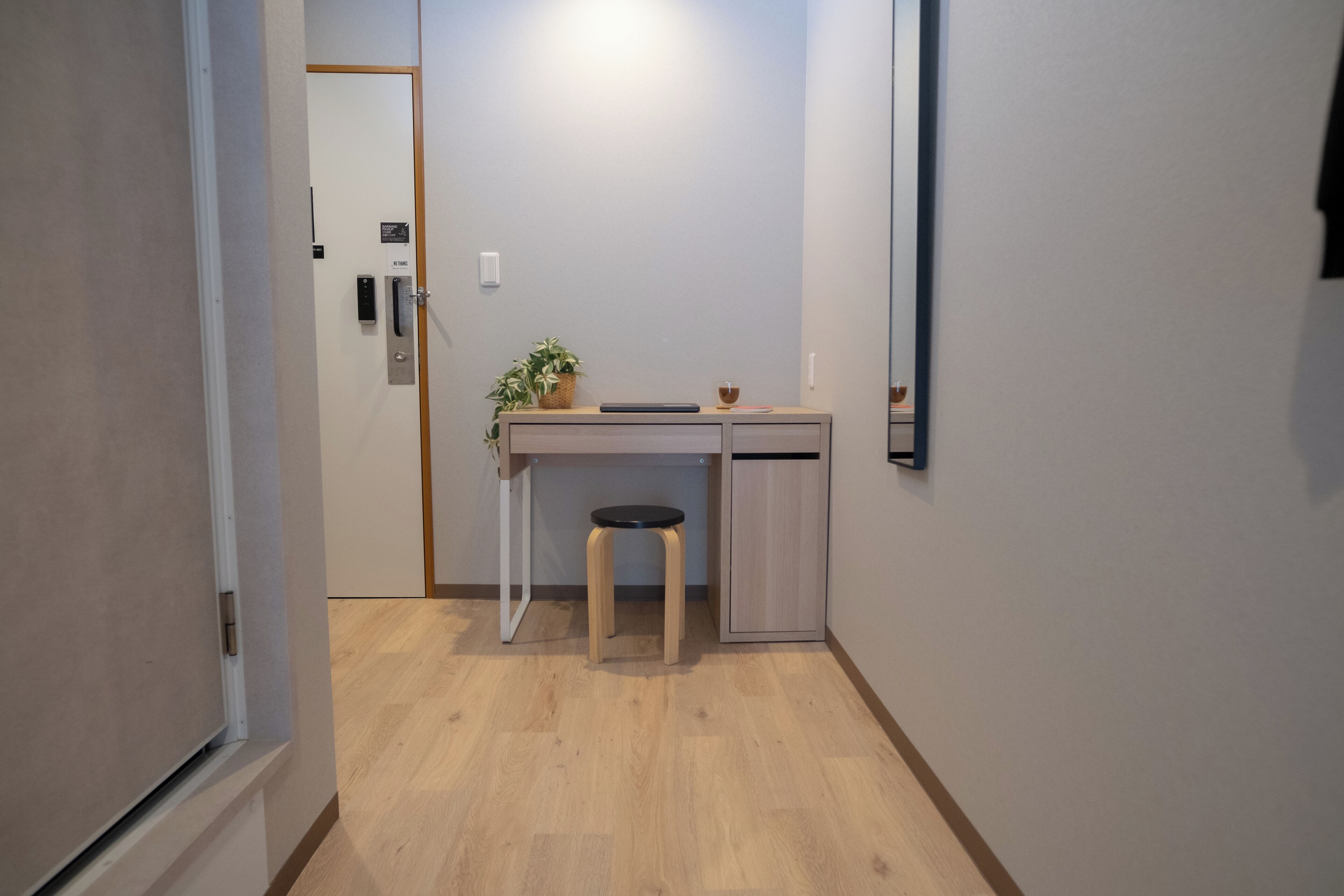 A small, modern room with a wooden desk, a stool, a potted plant, and a cabinet.