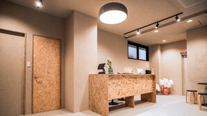 A reception area with a wooden reception desk, a potted plant, and a window. - Wayfarer Hotel Kyoto Shijo (Kyoto)