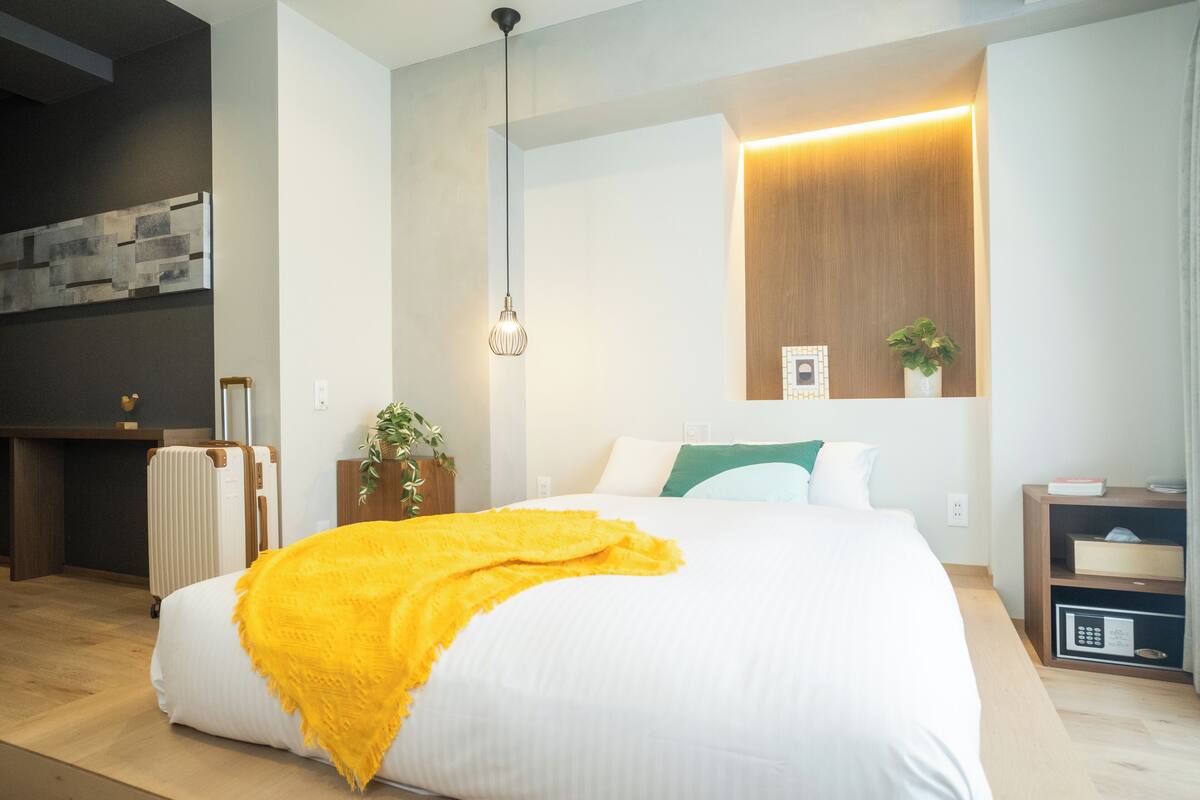 Ein modernes Hotelzimmer mit einem großen Bett, einem Holzkopfstück, einem Nachttisch mit Lampe, einem Wandregal mit Dekoration und Blick auf die Stadt.