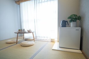 Una stanza in stile giapponese minimalista con pavimento in tatami, un tavolino con set da tè, un frigorifero e una pianta in vaso.