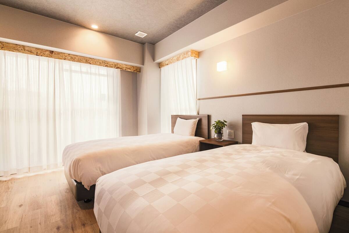 Ein Hotelzimmer mit zwei Betten, Holzboden, einem Nachttisch mit Pflanze und einer Wandleuchte.