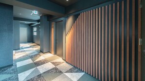 A modern hallway with a geometric patterned floor, a wooden slatted wall, and a door with a sign indicating a 9F destination. - Wayfarer Hotel Kyoto Shijo (Kyoto)
