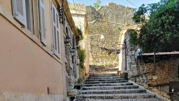 Un escalier en pierre mène à un bâtiment doté d’un mur en pierre, et on peut apercevoir une colline en arrière-plan.
