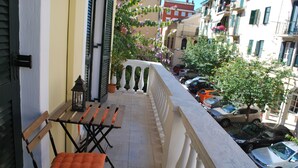 Un balcon avec une table et des chaises en bois, un pot de fleurs et une vue sur les voitures garées et les immeubles.