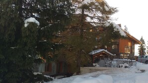 A wooden lodge with a stone facade, surrounded by snow-covered trees and a snow-covered driveway.