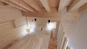A wooden cabin bedroom with a bed, bedside tables, and a window.