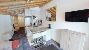 A modern kitchen with stainless steel appliances, a dining area with a bar stool, and a TV mounted on the wall.