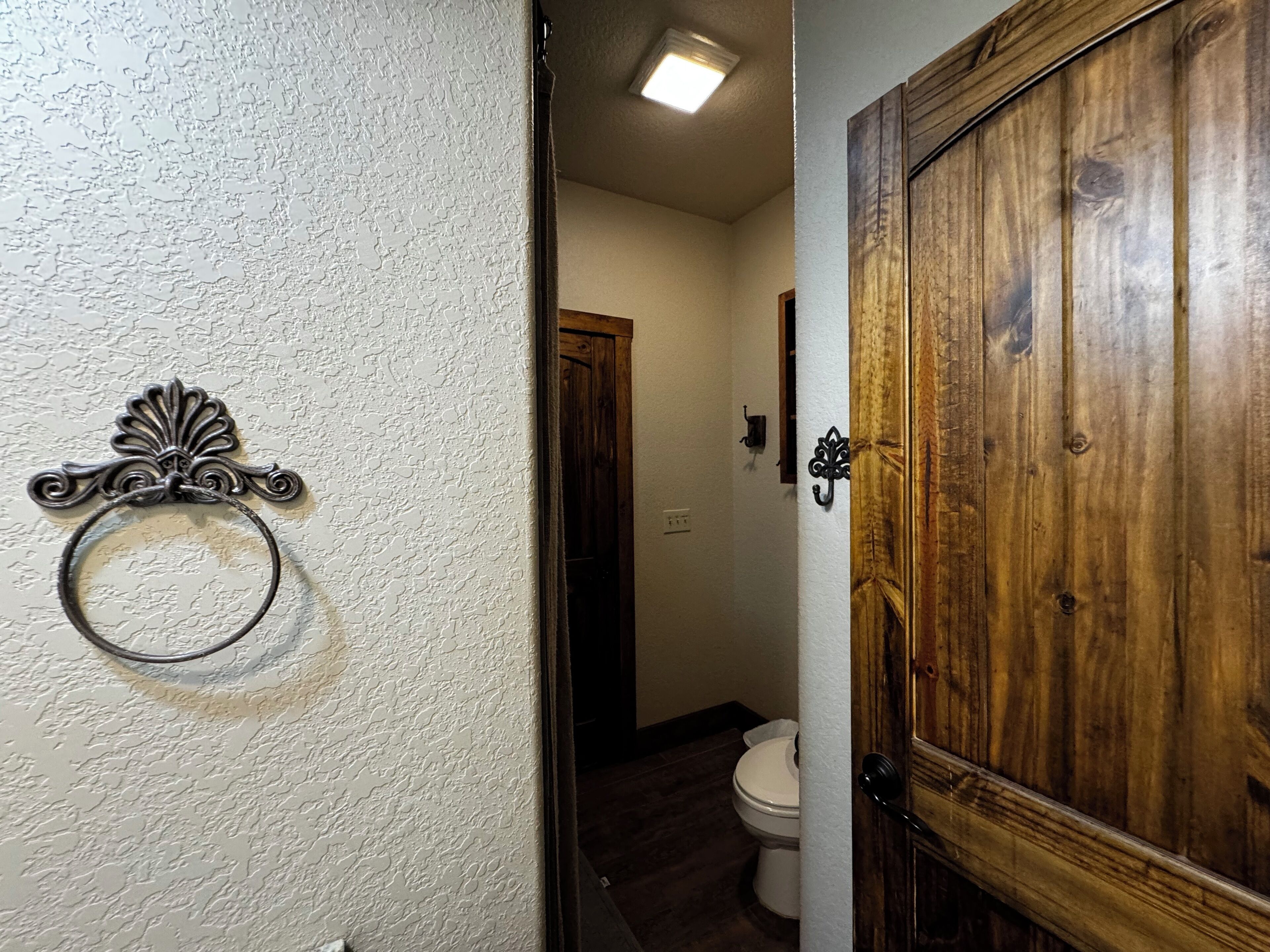A hallway with a wooden door, a white textured wall, and a toilet visible in the background.