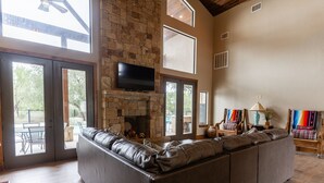A spacious living room with a stone fireplace, large windows, and a leather sofa. - Soak up the Sun and Golf Course Views from The Sweet Spot! (Concan)