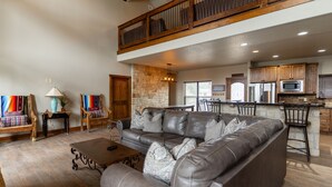 A spacious living room with a leather sectional sofa, a wooden dining table, and a kitchen area with stone walls and wooden cabinets. - Soak up the Sun and Golf Course Views from The Sweet Spot! (Concan)