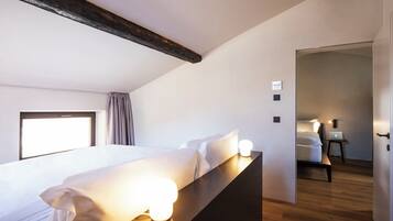 Habitación de hotel moderna con una cama grande, lámparas de noche, cabecera de madera y vista a otra habitación.