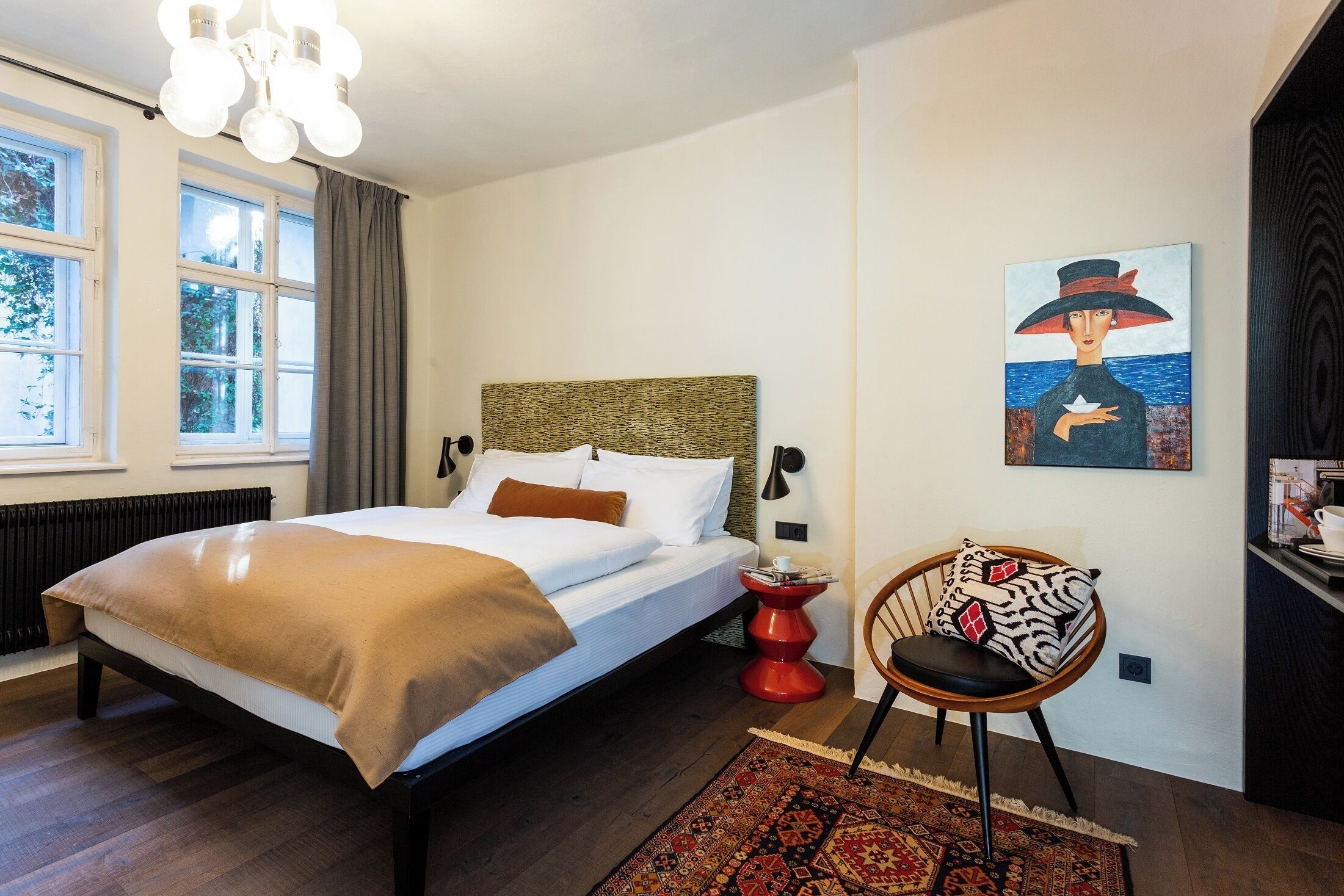 Un dormitorio con una cama, una silla, un cuadro y una ventana.