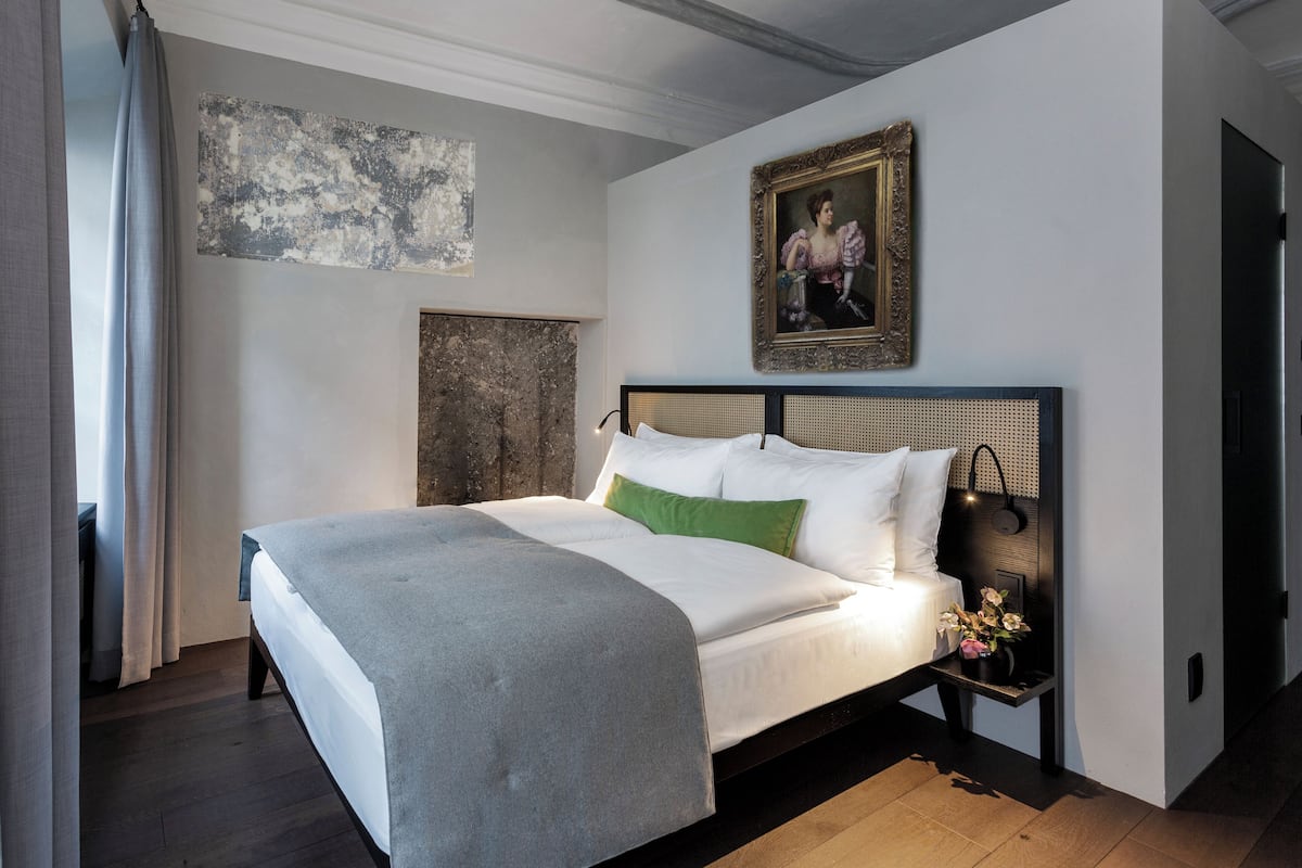 A bedroom with a bed, a nightstand, a painting, and a wall with a textured artwork.
