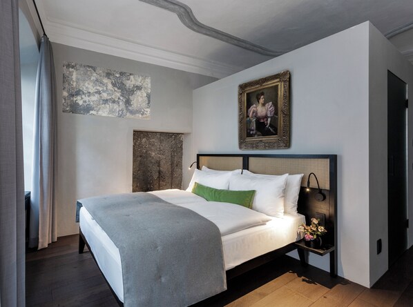 A bedroom with a bed, a nightstand, a painting, and a wall with a textured artwork. - Goldenstern Townhouse (Bolzano)