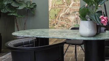 A table with a map mural, a potted plant, and a black chair in a room with stone flooring.