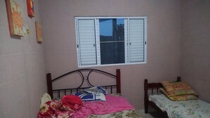 Een slaapkamer met een eenpersoonsbed, een kleiner bed en een raam met luiken.