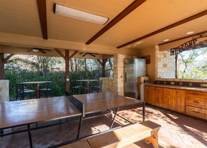 An outdoor patio with a ping pong table, stone walls, and a refrigerator.