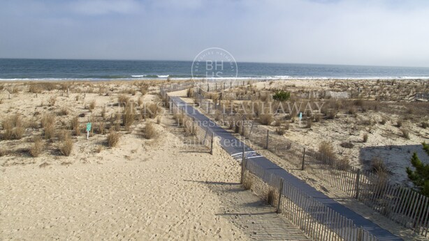 A beach pathway leading to the ocean, surrounded by sandy dunes and sparse vegetation.