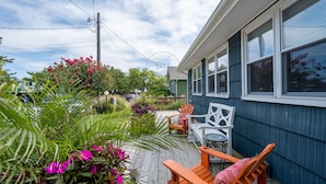 A wooden deck with outdoor seating, surrounded by lush greenery and flowering plants.