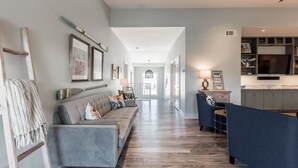 Un salón espacioso con un sofá gris, un sillón azul y suelo de madera.