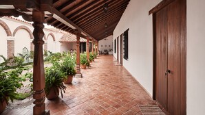 A covered corridor with tiled flooring, wooden columns, potted plants, and a door on the right.
