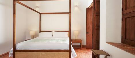 Una cama con dosel de madera, dos lámparas de noche y un pequeño taburete de madera.