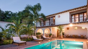 A pool area with lounge chairs, a dining area, and a building with a balcony.