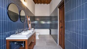 A modern bathroom with blue-tiled walls, a wooden vanity, a bathtub, and two mirrors.