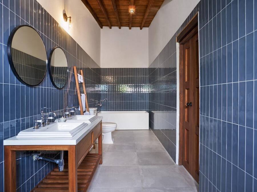 A modern bathroom with blue-tiled walls, a wooden vanity, a bathtub, and two mirrors.